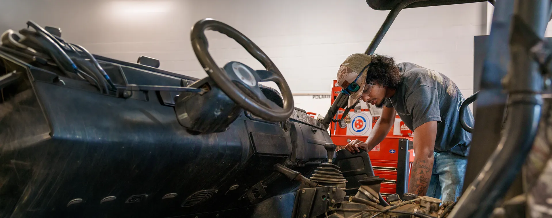 Person inspecting the dashboard area of a utility vehicle inside a powersports training shop.